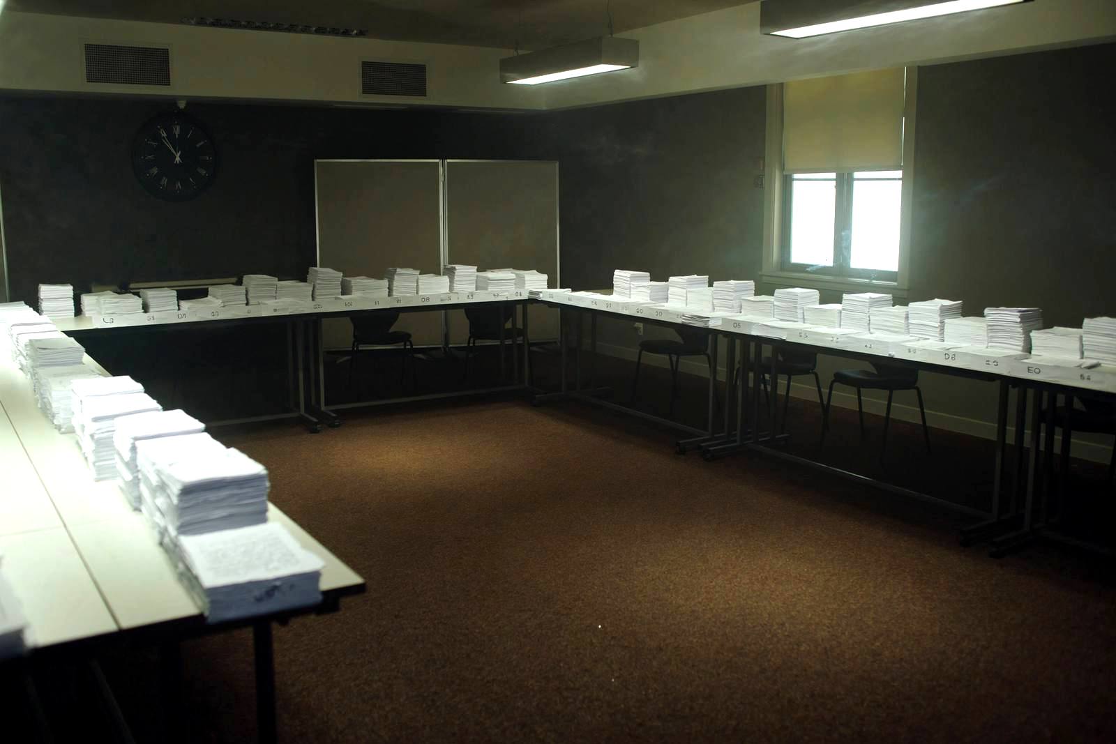Dossiers de candidature numérotés disposés sur de longues tables dans une salle d'examen